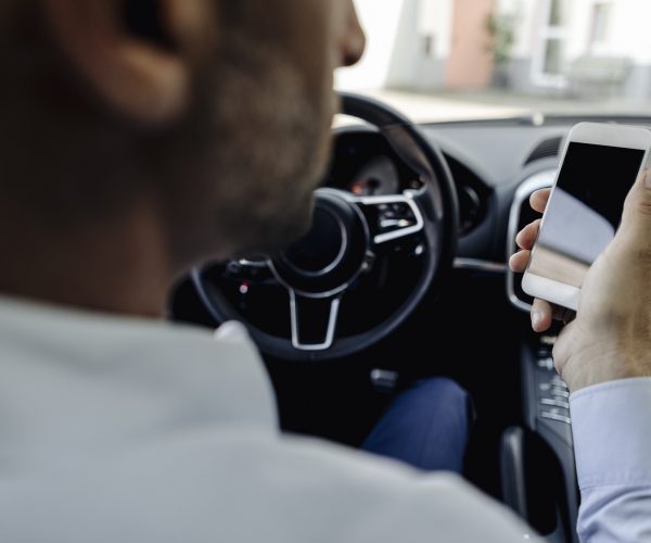 Businessman driving car looking at cell phone